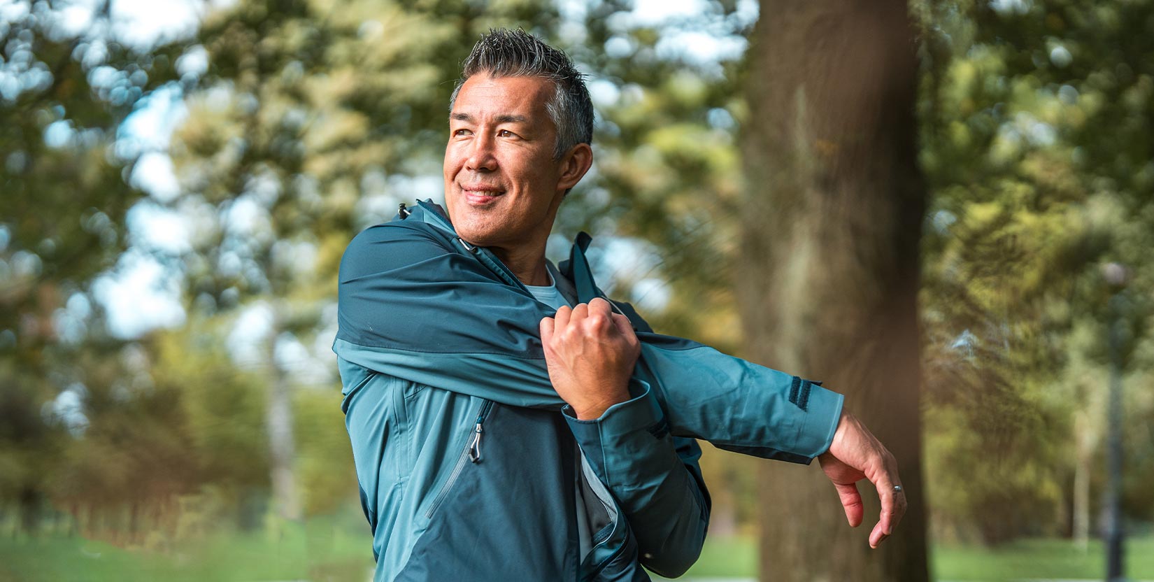 Phase1 PT Services An Asian man in his mid-adult years practices outdoor fitness by stretching in a public park.