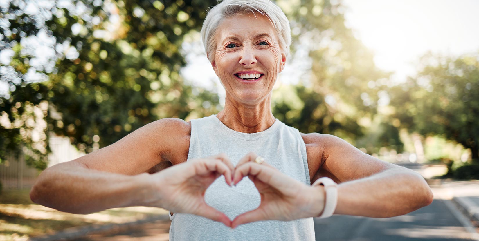BACK-AND-NECK-PAIN-TREATMENT Fitness, happy and heart hands of old woman in nature after running for health, wellness and workout. Smile, motivation and peace with senior lady and sign for love, faith and training in nature